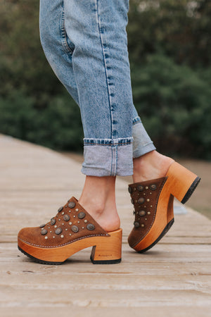 Modelo Pájaro Pastora Renobuk Tostado, sandalia tipo zueco artesanal de Kebba. Cuero renobuk tostado con tachas decorativas, planta de madera álamo de 8 cm y forro de cuero caramelo. Imagen lateral sobre fondo blanco. Piezas únicas en colecciones limitadas. Hecho a mano en Villarrica. Kebba: tradición y herencia en tus manos